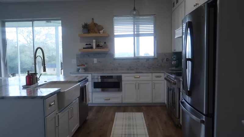 A Modern Kitchen Featuring Sleek Stainless Steel Appliances, White Cabinetry, Marble Countertops, and Floating Shelves, Offering a Clean and Affordable Update with Contemporary Finishes